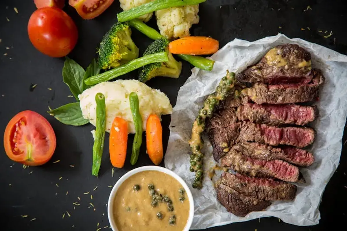 Grilled steak served with fresh vegetables and pepper sauce, creating a colorful and appetizing meal.