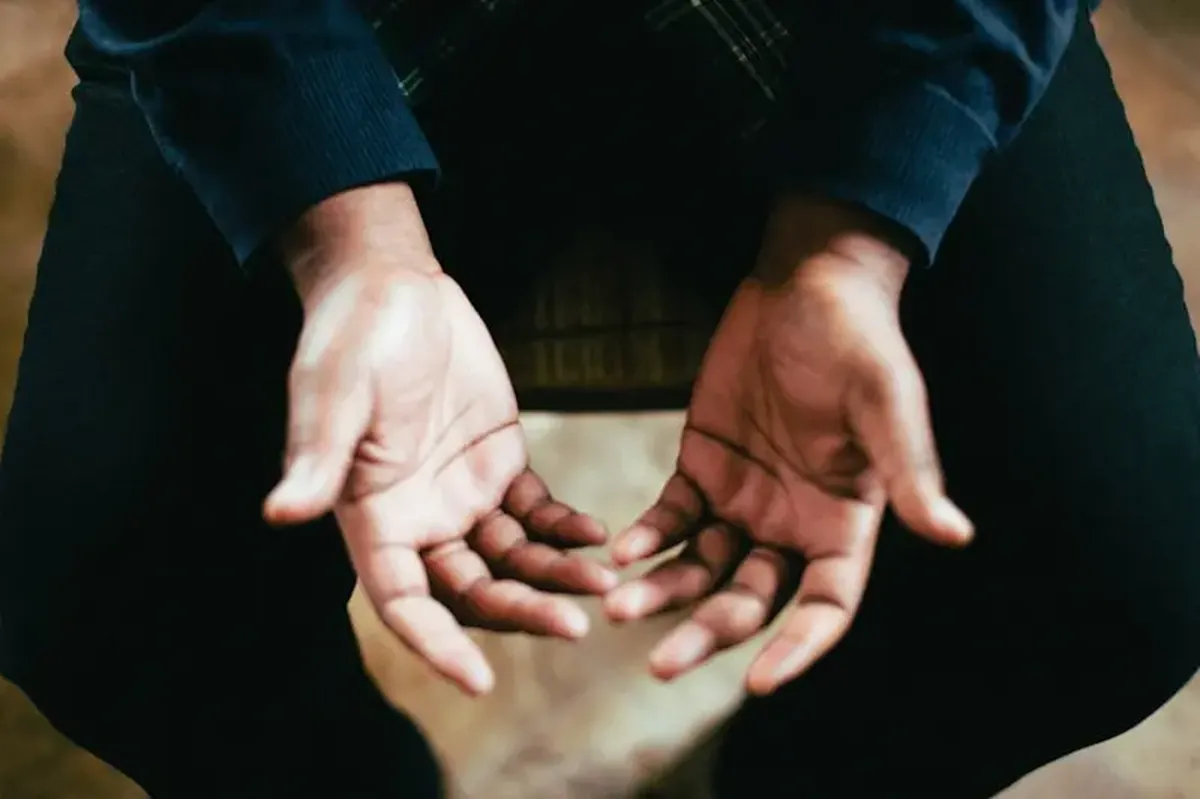 A person showing both palms while sitting on a chair.