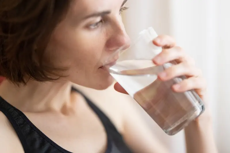 Why Drinking Water Alone Won't Quench Your Summer Thirst 3 A woman in a black tank top drinking water.