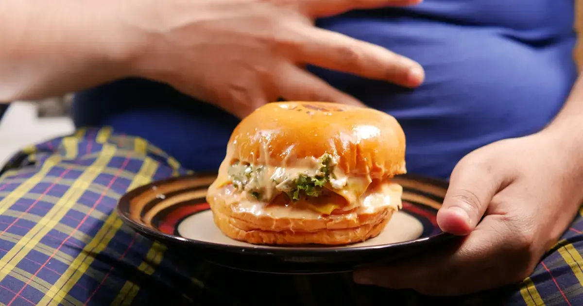How Lack of Sleep Sparks Dozens of Life-Threatening Diseases 6 An overweight person holding a hamburger