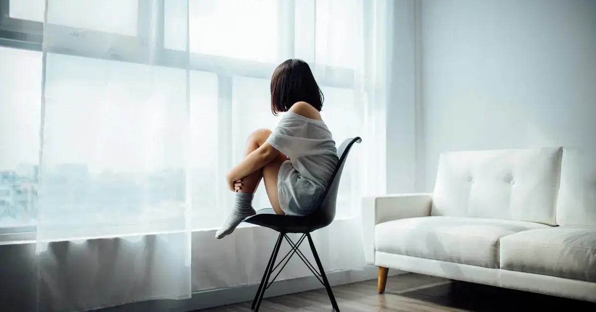 A woman sits on a chair, hugging her knees.