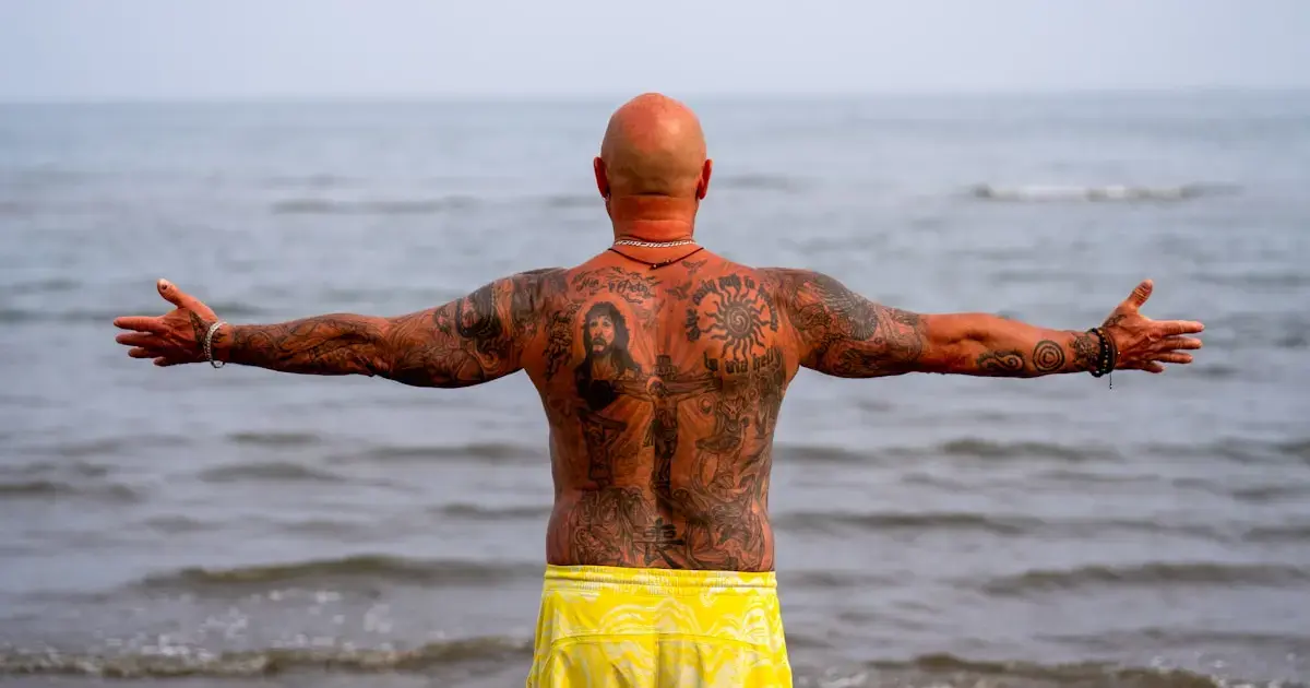 A man with a tattoo on his back by the sea.