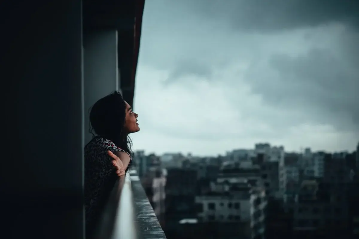 A woman on a balcony watching the rain.
