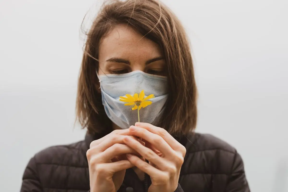 How Bad Smells Harm Your Body and Mind 5 A woman smelling a flower while wearing a mask