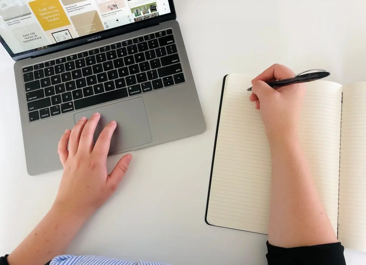 Person working on a laptop and writing by hand